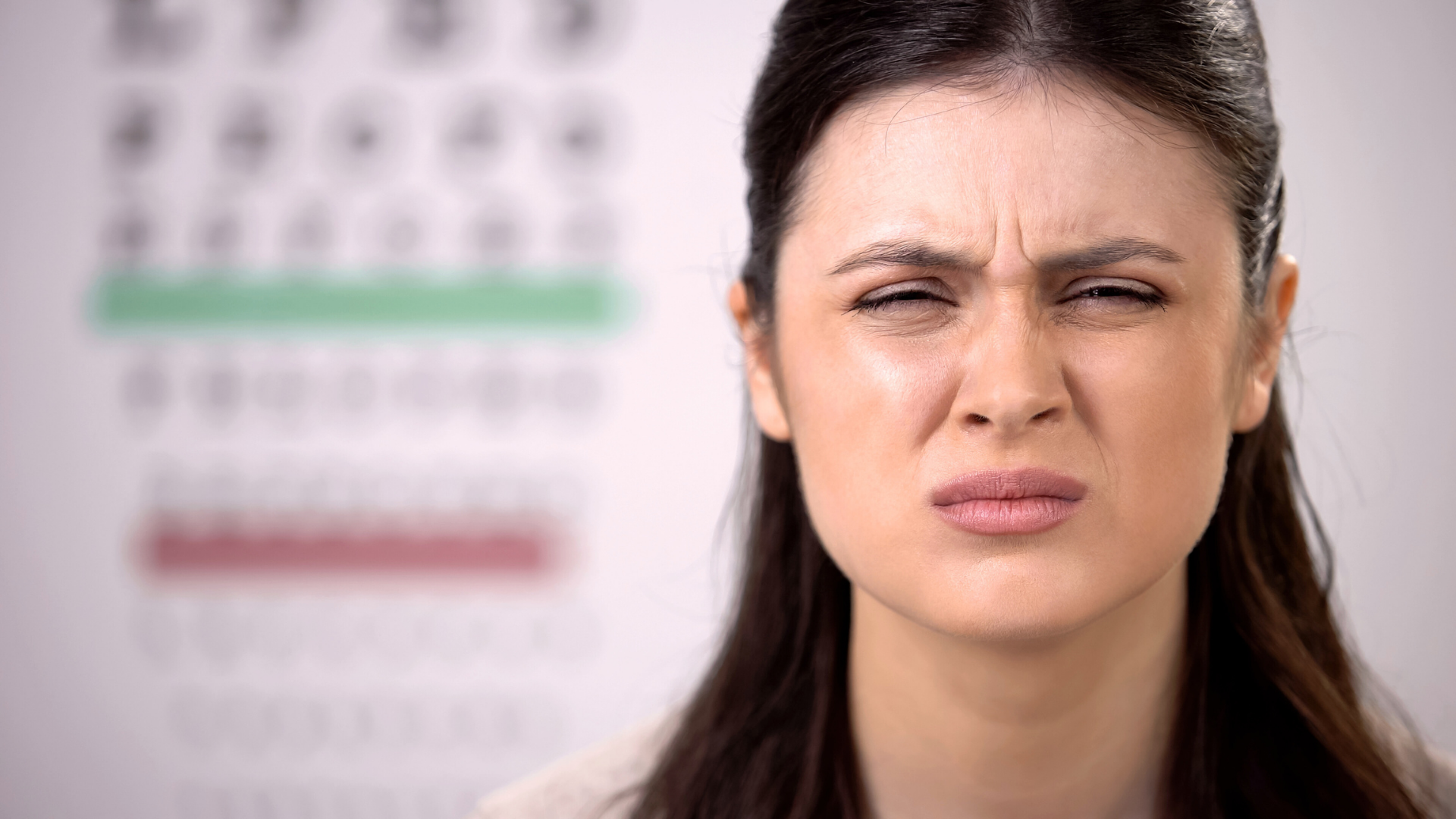 Ragazza con in sottofondo la tabella dell'oculista con le lettere che strizza gli occhi per vedere meglio