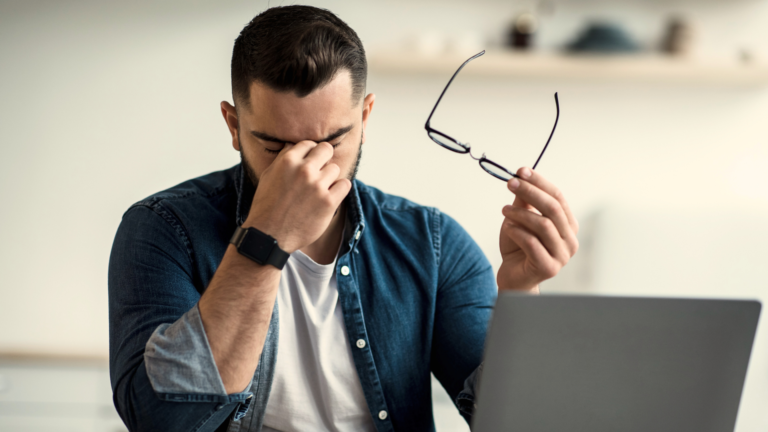 Ragazzo davanti al computer con gli occhiali in una mano e con l#altra si strofina gli occhi